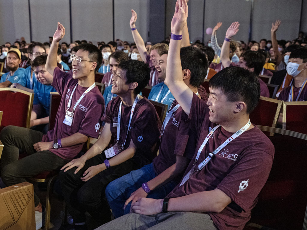 The team of three MIT programmers, and their student coach Ce Jin, smile broadly and raise their hands in celebration.