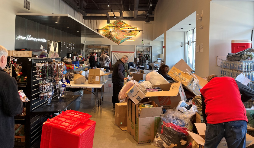 A staffer in a red vest digs through a large pile of cardboard boxes, plastic bags, and other containers filled with donated items.