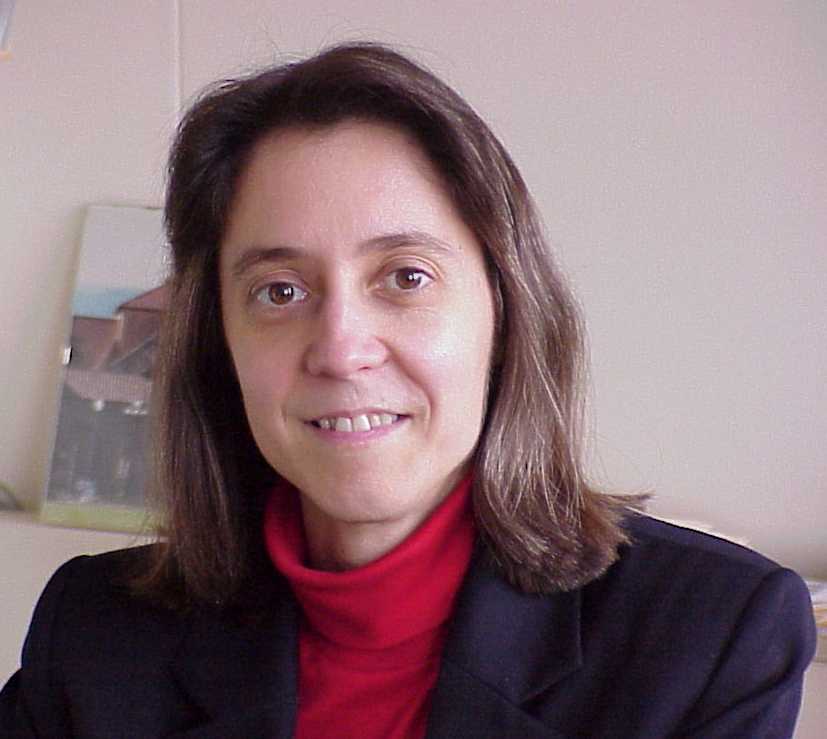 Judy Hoyt, seen here in her office in front of a photo of Stanford's campus, wears a red turtleneck and black blazer.