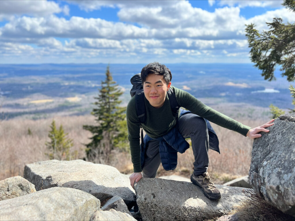 Student Christopher Wang is shown clambering over the edge of a high mountain summit.