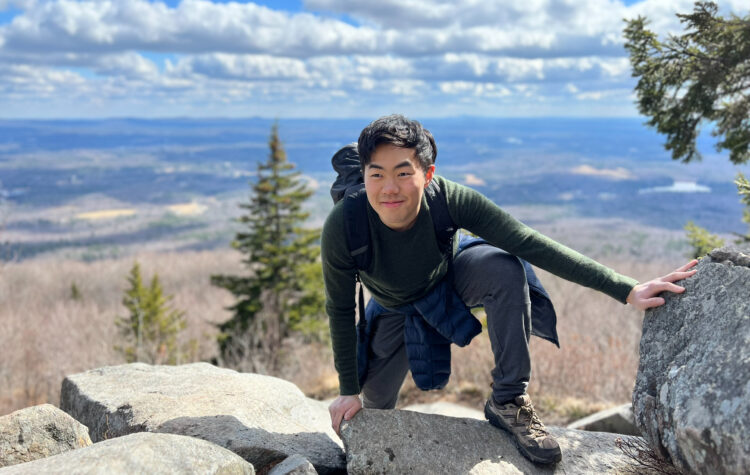 Student Christopher Wang is shown clambering over the edge of a high mountain summit.